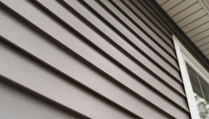 Close up look at greyish brown vinyl siding on a home with white windows.