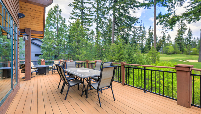 Beautiful large cabin home with wooden deck and chairs with table overlooking trees in the forest