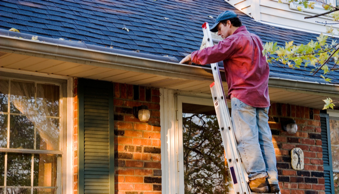 Man with red shirt Cleaning Gutters on Ladder