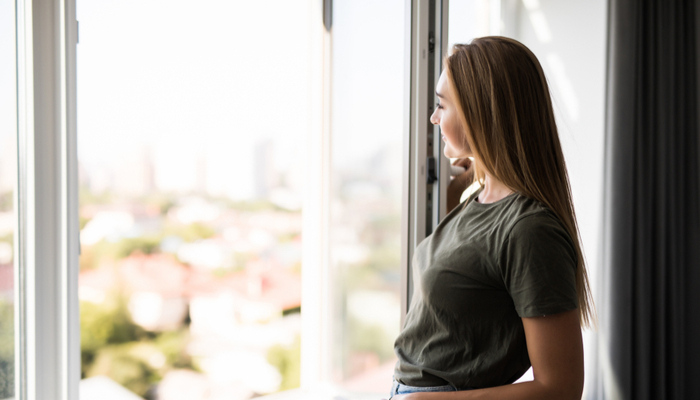Young woman smiling opening window in living room in summer weather