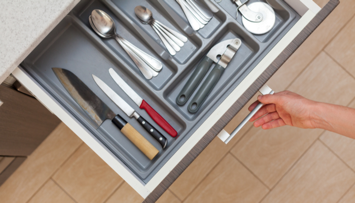 High angle top view photo of woman hand opening kitchen drawer by door handle, with different cutlery or utensils like spoon, knife, fork and stuff