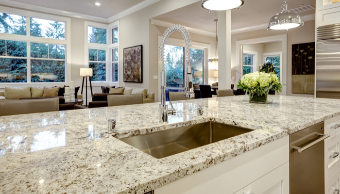 White kitchen remodel design features with large bar style island with granite countertop illuminated by modern pendant lights