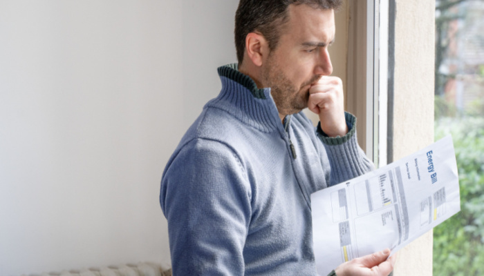 Man in blue sweater worried about bills reading energy increase costs beside the window