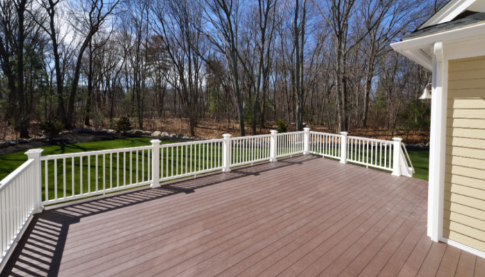 New backyard deck with white vinyl railings and composite brown boards with a view to the woods