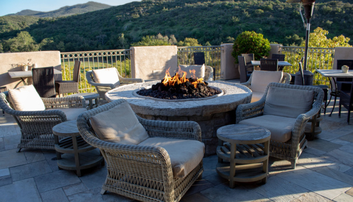Chairs with cushions and side tables around fire pit for gathering with trees and mountains on the background