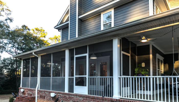Side view of a large two story blue gray house with wood and vinyl siding and a screened porch photo taken on a bright sunny day