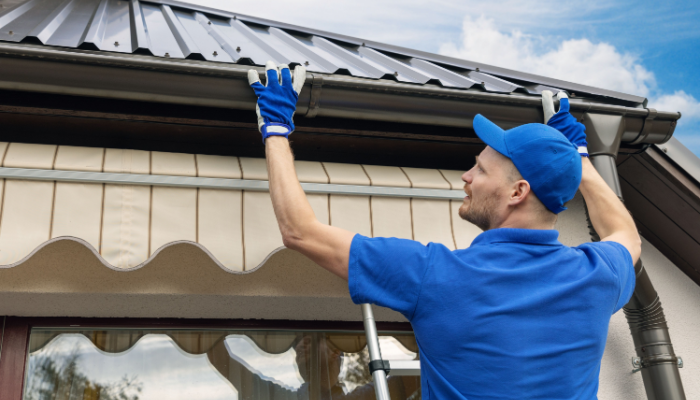 Roofer in blue shirt and cap installing house roof rain gutter system