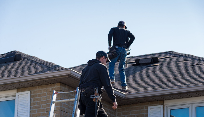 Two roofers in jackets and caps inspecting a damaged roof