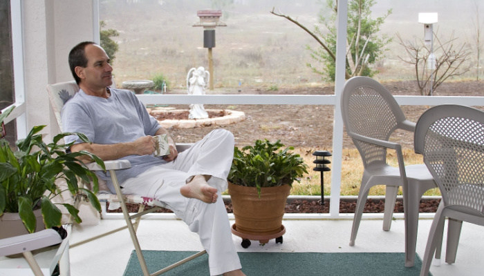 Man in bare feet enjoys his morning coffee in screened porch in the morning