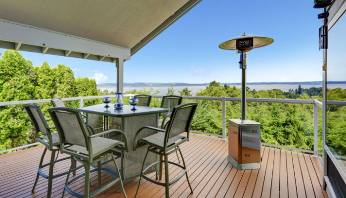 Patio area with table, chairs and heater on walkout deck overlooking scenic view with trees, mountains, and the ocean
