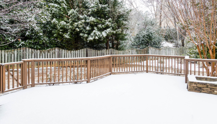 Snow on wood deck and fence with evergreens in background in the winter season
