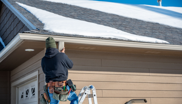 Contractor in black hoodie jacket installing gutters on a residential building in during winter season with snow on the roof