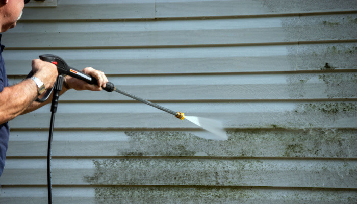 A man uses a power washer to clean mold and grime off the siding of a house caused by the cold weather of winter months