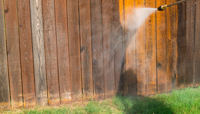 A person using high pressure power washer spraying and cleaning wooden fence to make it look new of winter months