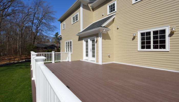Large, spacious, new construction composite deck in house backyard with brown boards, white railing posts and veranda